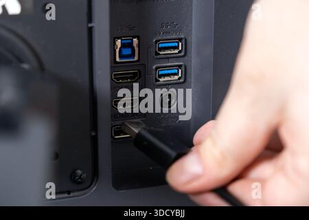 Top view of a hand connecting a black cable to a display device's rear panel, emphasizing available HDMI, USB, and DC-IN ports for various peripheral Stock Photo