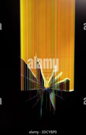 A severely cracked electronic display with a bright yellow background, showing numerous vertical color lines and a sharp impact point, illustrating da Stock Photo