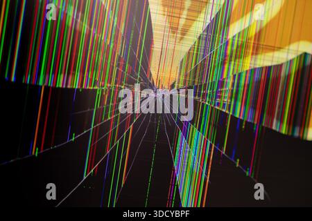 Detailed view of a severely cracked LCD screen with an impact point, showcasing vibrant vertical RGB color lines, representing device breakdown, syste Stock Photo