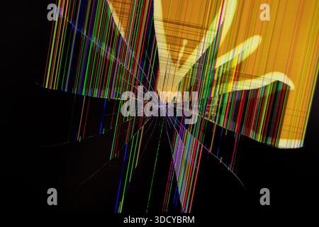 Close-up of a damaged digital screen with a central impact point, creating splintered glass patterns and a chaotic display of multi-colored pixel line Stock Photo