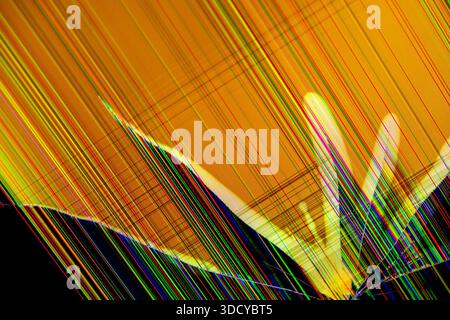 Close-up view of a broken digital screen with an orange background, featuring bright multicoloured lines and intricate cracks representing data corrup Stock Photo