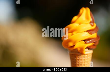 Swirled chocolate and orange soft serve ice cream in a waffle cone. Stock Photo
