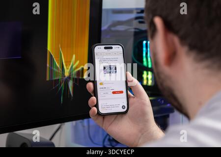Poznan, Poland - November 2, 2025: Close-up of a person's hand holding a smartphone to browse online stores for a replacement for their broken desktop Stock Photo