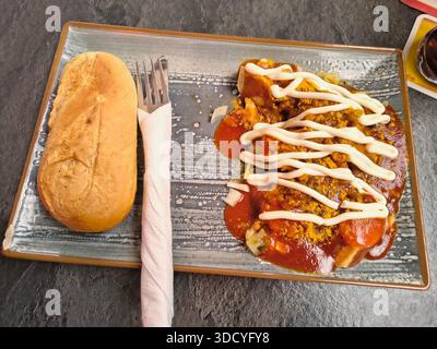 A delicious currywurst with mayonaise and a bread roll on a grey plate. Stock Photo