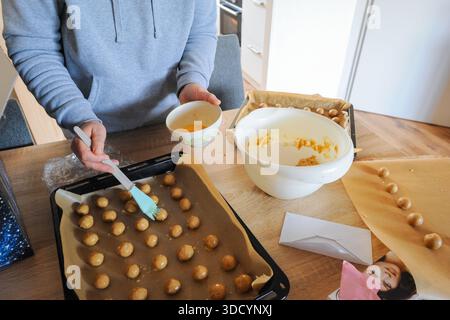Person placing raw cookie dough on a baking sheet, preparing homemade biscuits in a domestic kitchen Stock Photo