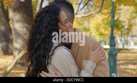 Hispanic glad couple talking positive in autumn park hugging cuddling guy and girl holding hands talk on street in fall autumnal city married spouses Stock Photo