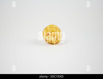 Macro closeup of single round caramel popcorn kernel centered on white surface, minimalist sweet snack concept for logo mockup Stock Photo