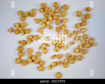 Top view of many round caramel popcorn pieces scattered across a white surface, sweet crunchy snack pattern for packaging, poster design Stock Photo