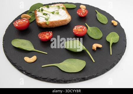 Toast with cream cheese spinach cherry tomatoes and cashew nuts on slate Stock Photo