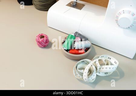 Sewing supplies including colorful thread spools, scissors, and a tape measure on a workbench Stock Photo