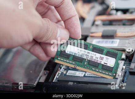 The precise moment of aligning a DDR3 SODIMM RAM stick with the motherboard slot pins during a computer repair. Focus on the connection interface. Stock Photo