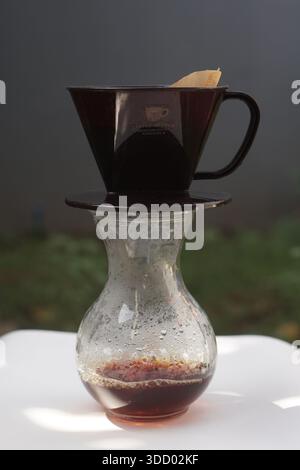 A glass coffee server with a plastic dripper and paper filter, capturing the steam and condensation of freshly brewed coffee. Lifestyle and beverage p Stock Photo