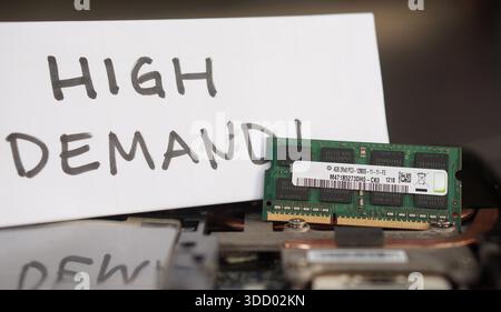 A DDR3 RAM stick resting on a laptop with a handwritten "HIGH DEMAND!" sign. Represents the global scarcity of electronic parts and supply chain bottl Stock Photo