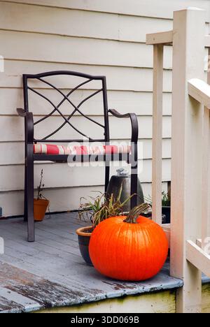 A Halloween pumpkin stands on a wooden porch in front of a chair at a historic home in Wilton Connecticut on an autumn Stock Photo