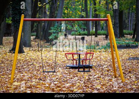 An empty children's swing on a chain against a backdrop of autumn leaves in an autumn park. Blurred background. Playground in the park. Stock Photo