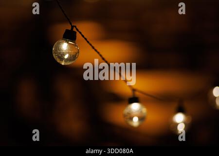 Round glass bulbs of a garland against a dark background. Focus on one bulb. Warm bokeh. Warm reflections. Stock Photo