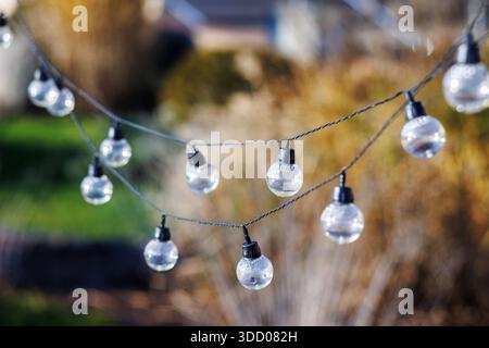 A garland of hanging lit light bulbs during the day. The bulbs have water droplets inside. Round bulbs on a black cable. Stock Photo
