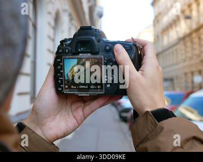 Close-up view of a photographer holding a DSLR camera and shooting urban architecture on a city street. Concept of street photography, travel photogra Stock Photo