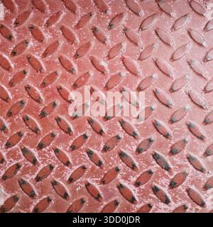 A top-down view showing the raised diamond pattern on a weather-worn red painted metal floor plate. Stock Photo