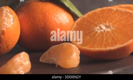 A close-up, low-angle still life of vibrant, whole, and halved mandarin oranges and loose segments, showcasing the juicy texture and bright orange col Stock Photo