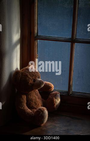 Teddy bear on the windowsill with glass covered in droplets Stock Photo