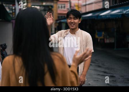 Young asian man greeting woman with a smile and wave on an urban street Stock Photo