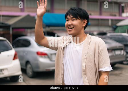Young asian man waving hand, smiling cheerfully, greeting someone in city street Stock Photo