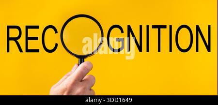 Hand holding magnifying glass examining the word recognition on yellow background Stock Photo