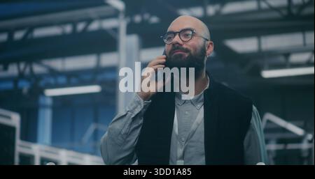 IT Manager Actively Discussing Problem on Phone in Data Center. Bearded IT Manager Actively Talks and Gestures on Smartphone in Server Hall. Urgent Problem Solving, and Technical Crisis Management. Stock Photo