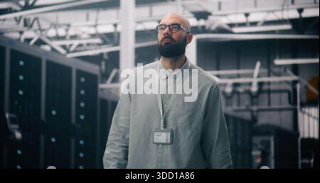 Cloud Infrastructure Architect Oversees Massive Data Center Hall. Bearded Man Overseeing Operations Inside Massive, Clean Data Center. Concept of Scale of Cloud Architecture and Big Data Management. Stock Photo