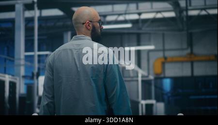 Engineer Walking Through Tech Enterprise Center. Bearded Professional Walking Steadily Through Brightly Lit Hall of Large Tech Enterprise Center. High Tech Work Environment and Maintenance Rounds. Stock Photo
