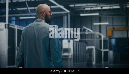 Engineer Inspecting Data Center Hall. Male IT Specialist Walks Through Massive Server or Industrial Hall. Emphasizes Facility Inspection, Professional Walking, and Scale of Infrastructure. Back View. Stock Photo