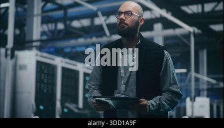 Engineer Checking System Metrics on Digital Tablet. Bearded IT Engineer in Dark Vest and Glasses Monitors System Metrics on Digital Tablet Amidst Server Racks. Cloud Auditing, and Technical Analysis. Stock Photo