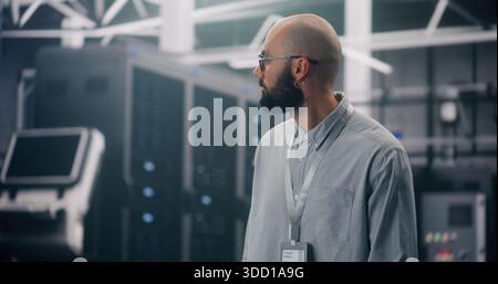 IT Professional Inspecting Rows of Active Server Racks. Male Engineer Walks Large Data Center, Conducting Physical Inspection of Glowing Server Racks. Security Protocol, Infrastructure Surveillance. Stock Photo