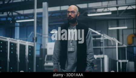 Internal Audit Specialist Inspecting Equipment in Industrial Server Space. Man in Professional Attire Performs Audit While Walking Across Server Units. Concept System Analysis, Technical Inspection. Stock Photo