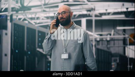 Data Center Manager Taking Critical Business Call. IT Specialist in Server Hall Handling Critical Business Call on Smartphone. Concept Client Liaison and Professional Communication in IT Management. Stock Photo