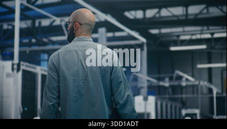 Engineer Walking Through Tech Enterprise Center. Bearded Professional Walking Steadily Through Brightly Lit Hall of Large Tech Enterprise Center. High Tech Work Environment and Maintenance Rounds. Stock Photo