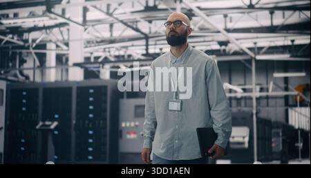 IT Engineer Walking Through Server Racks in Modern Data Center. Focused Man With Badge and Laptop Walking Among Rows of Glowing Server Racks. Concept of IT Infrastructure and Cloud Technology. Stock Photo