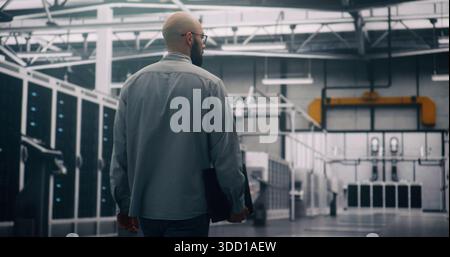 Professional Inspecting IT Infrastructure. Bearded Engineer Walks Between Rows of Servers, Seemingly Conducting Silent Technical Audit of Cloud Architecture. Technical Control and System Integrity. Stock Photo