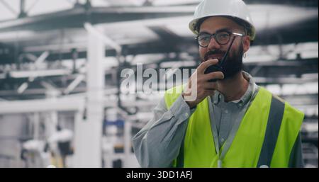 Factory Foreman Using Radio For Urgent Communication. Man in Safety Helmet Using Walkie Talkie For Urgent Communication on Noisy Production Floor. Concept Clear Communication and Site Supervision. Stock Photo