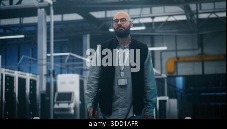 Professional Engineer Walking Through High Tech Facility. IT Supervisor in Dark Vest and Shirt Walks Purposefully Through Large Server Facility. Concept Professional Oversight, Monitoring and Control. Stock Photo