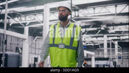 Engineer in Safety Vest Inspecting Production. Male Industrial Supervisor in Hard Hat Focused Inspecting Operations on IT Factory Floor. Industrial Safety, Production Management, Quality Control. Stock Photo