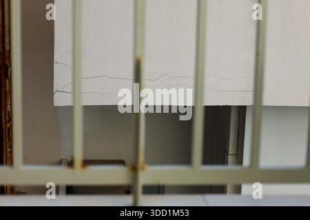 A cracked wall seen through rusted metal bars, evoking themes of confinement, neglect, and time's irreversible effects Stock Photo