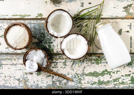 Variety of coconut products milk in glass bottle, oil and flakes in shell, fresh broken coconut on old wooden plank background. Healthy eating. Flat lay, space Stock Photo