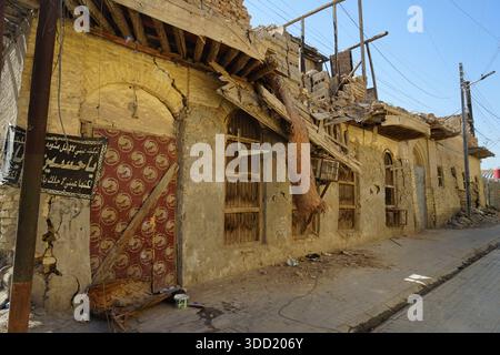 Damaged traditional mud-brick building in the old town of Basra, southern Iraq, showing severe structural decay, collapsed wooden roof beams, cracked Stock Photo