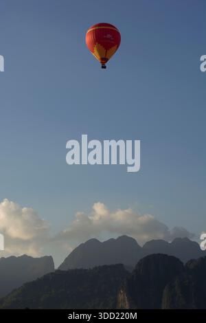 a red and yellow hot air balloon floats above limestone karsts in vang vieng, laos Stock Photo