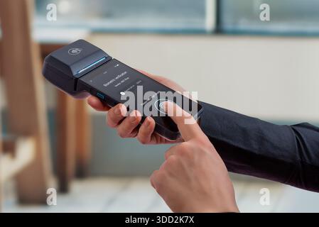 User confirming payment with biometric fingerprint verification on portable POS terminal, representing secure authentication, identity confirmation, a Stock Photo