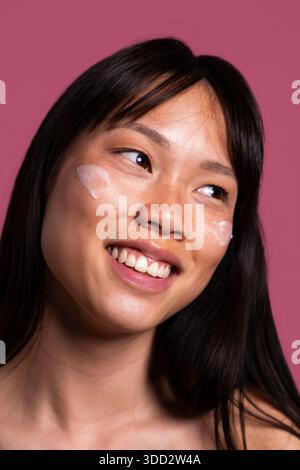 Beautiful chinese woman portrait on colorful background. Young asian woman smiling, showing fresh natural skin with cream applied, promoting beauty an Stock Photo