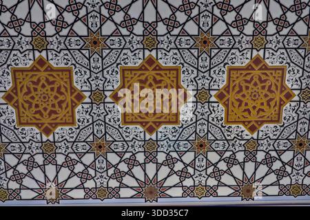 A vibrant, large-scale, repeating geometric pattern featuring golden-orange medallions and complex black-and-white star shapes across a white ceiling. Stock Photo