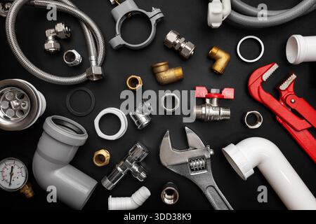 Plumbing tools and fittings on black background. Plumber equipment, top view Stock Photo